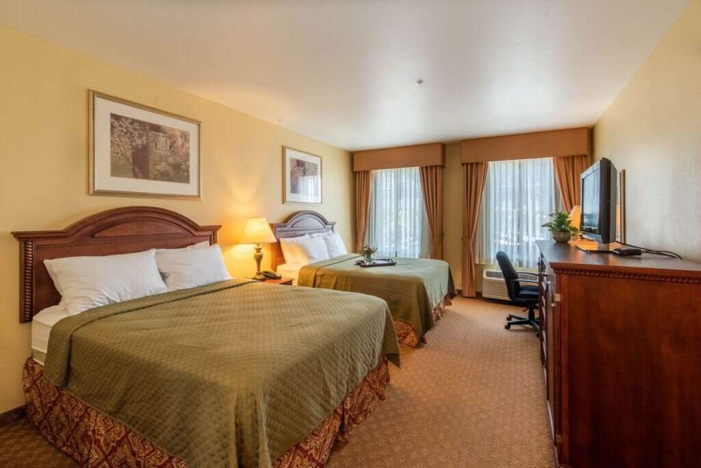 Hotel room with two double beds, TV, and desk.