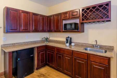 Corner kitchenette with dark wood cabinets, microwave, sink, mini-fridge, and wine rack.