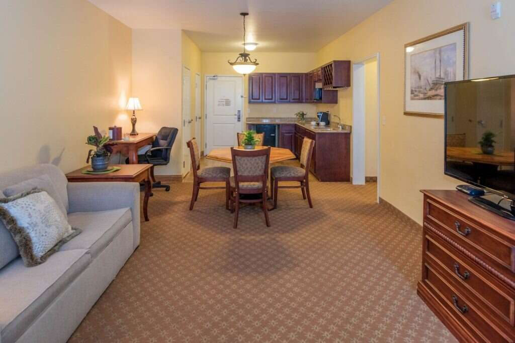 Cozy hotel suite with seating area, dining table, kitchenette, and TV.