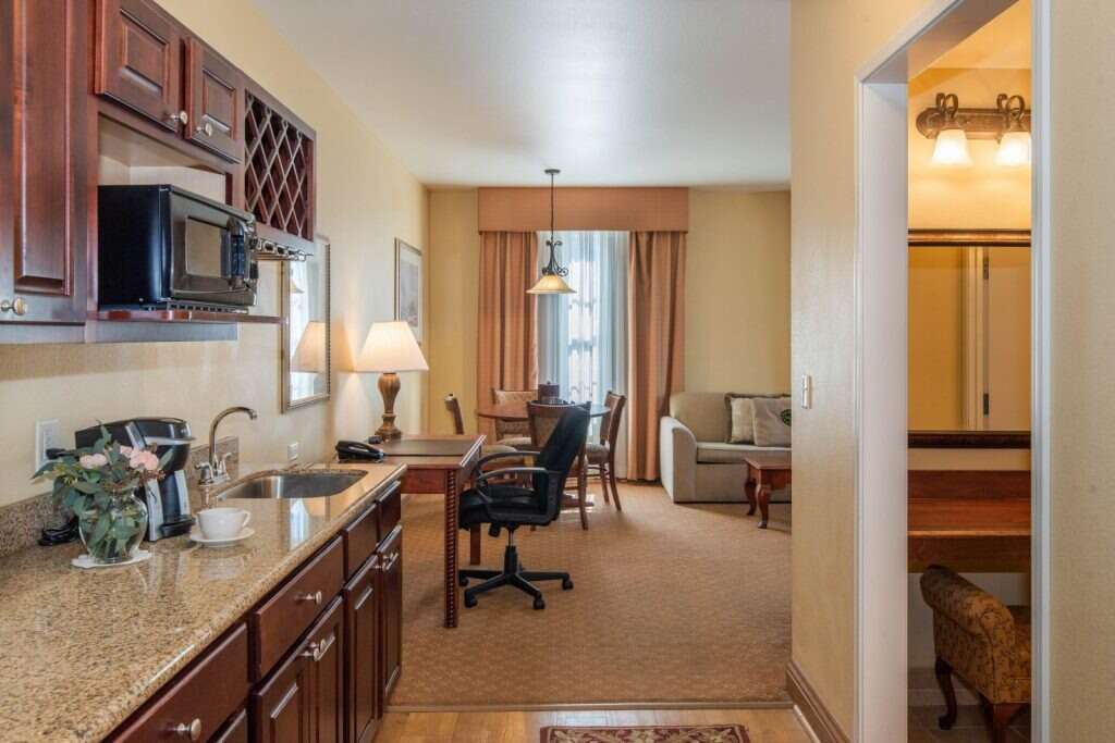 Kitchen area, dining table, and seating in a hotel suite with tan walls and brown accents.