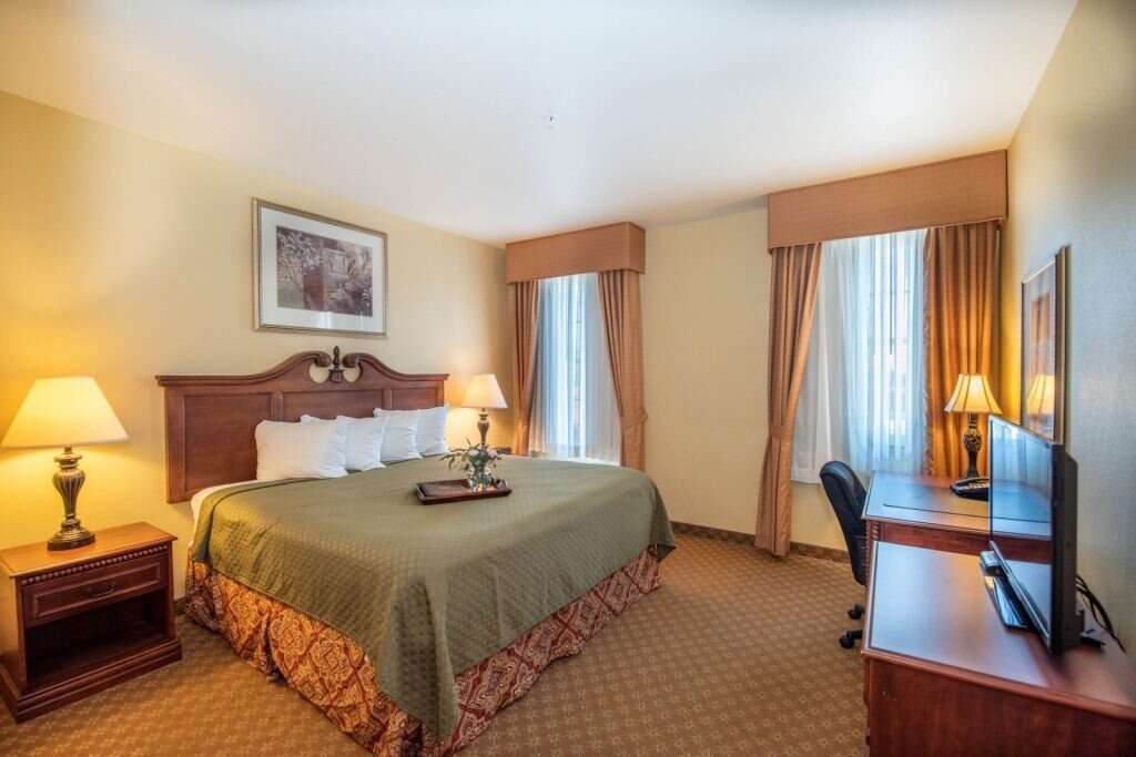 Hotel room with king bed, desk, lamps, and TV.
