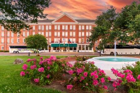 Hotel exterior with fountain, buses, and pink flowers against a sunset sky.