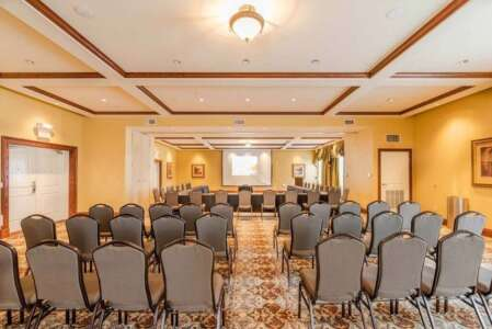Meeting room with rows of chairs facing a table with a projector screen; yellow walls, brown trim.
