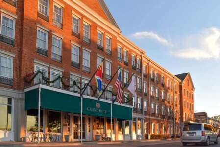 Hotel exterior with brick facade, green awning, and flags. A street with a vehicle passes by.