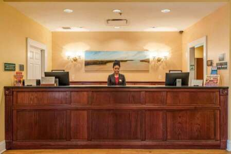 Hotel front desk; a woman stands behind a wooden counter, facing the viewer.