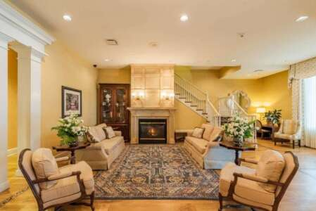 Elegant lobby with seating, fireplace, and staircase. Cream and gold tones with a floral rug and artwork.