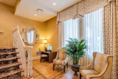 Interior hotel lobby with stairs, desk, chairs, mirror, and window.