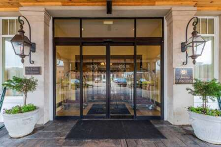 Hotel entrance with glass doors, flanked by potted plants and ornate sconces.