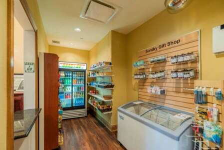 Small gift shop interior, yellow walls, wood floor. Refrigerator, shelves with snacks, and display of items.