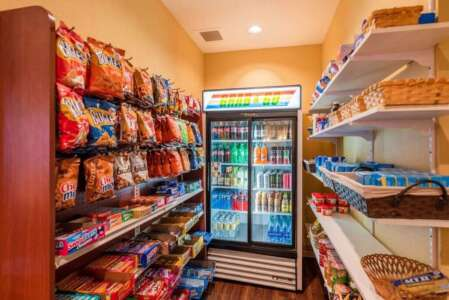 A brightly lit snack pantry with shelves of chips, candy, and a cold beverage refrigerator.