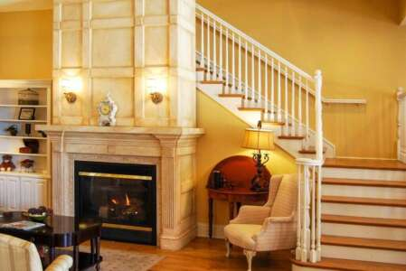 Fireplace, staircase, and chair in a living room with yellow walls and wood floors.