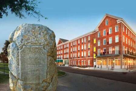 A large rock with an engraved sign stands in front of a red brick hotel.
