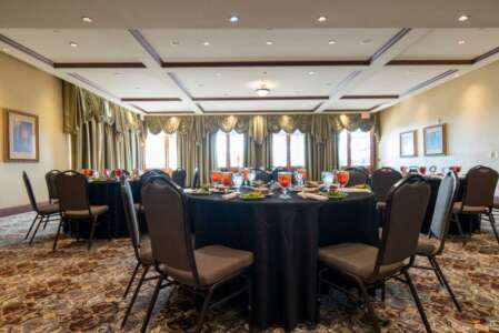 Round tables in banquet hall, set for a meal. Black tablecloths, brown chairs, and patterned carpet.