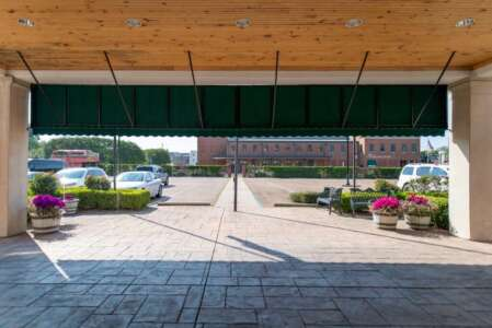 Green awning over a driveway, with cars parked and a building in the distance.