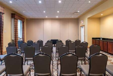 A conference room with rows of chairs facing a table, beige walls, and carpeted floor.