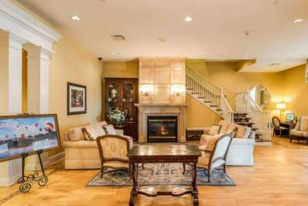 Lobby with fireplace, sofas, staircase, and art on a wooden floor. Warm tones, elegant setting.