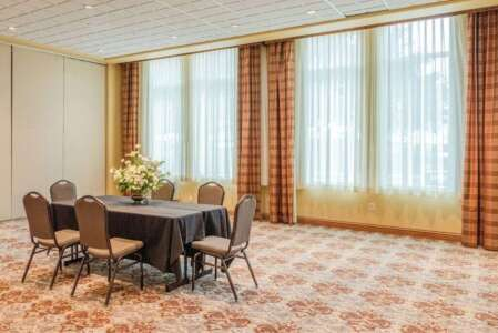 Meeting room with a table, chairs, large windows with drapes, and floral arrangement. Beige and brown tones.