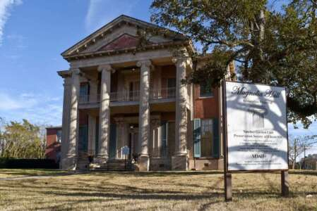 Historic mansion with large white columns, brick exterior, and sign in front.