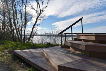 Wooden steps lead to a view of a bridge over a river on a sunny day.