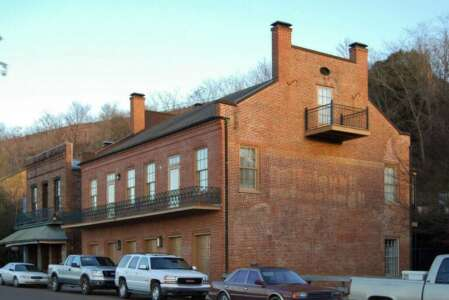 Red brick building with a balcony, parked cars in front, set against a hillside.