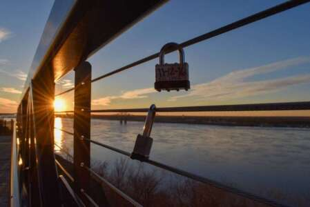 Sunset view through a bridge railing, with two love locks on a wire overlooking a river.