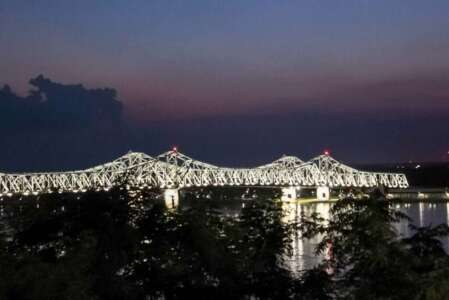 Lit-up bridge over water at dusk with purple and dark blue sky.