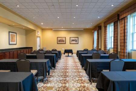 Conference room with tables and chairs set for a meeting. Black tablecloths, neutral walls, and patterned carpet.