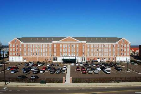 Large brick building with cars parked in front on a sunny day.