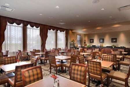 Hotel dining room with tables, chairs, and buffet area. Brown and beige tones.
