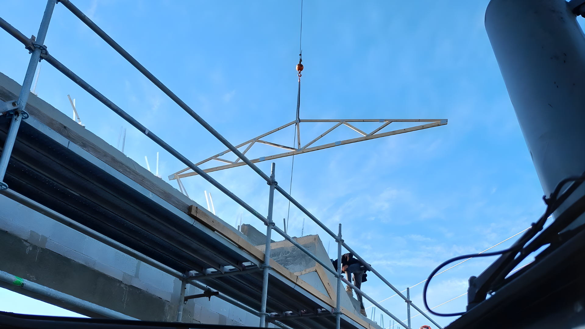 Construction crane lifting a beige truss on a building site under a clear blue sky