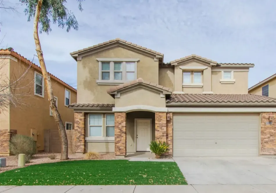 Two-story beige suburban house with a double garage, front lawn, and driveway