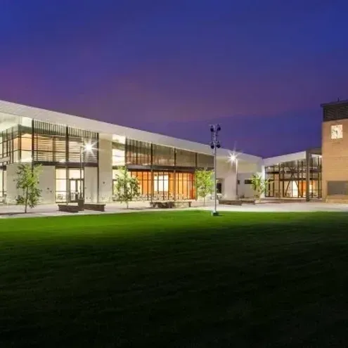 Modern glass building lit at dusk beside a green lawn under a purple sky