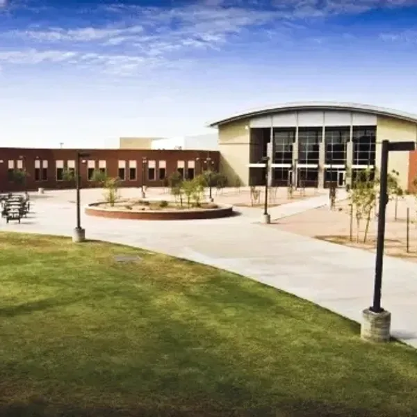 Modern campus courtyard with a large curved building, paved walkways, and grassy lawn under a blue sky