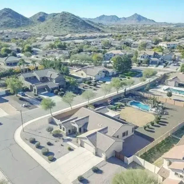 Aerial view of a suburban neighborhood with houses, streets, and desert mountains in the background