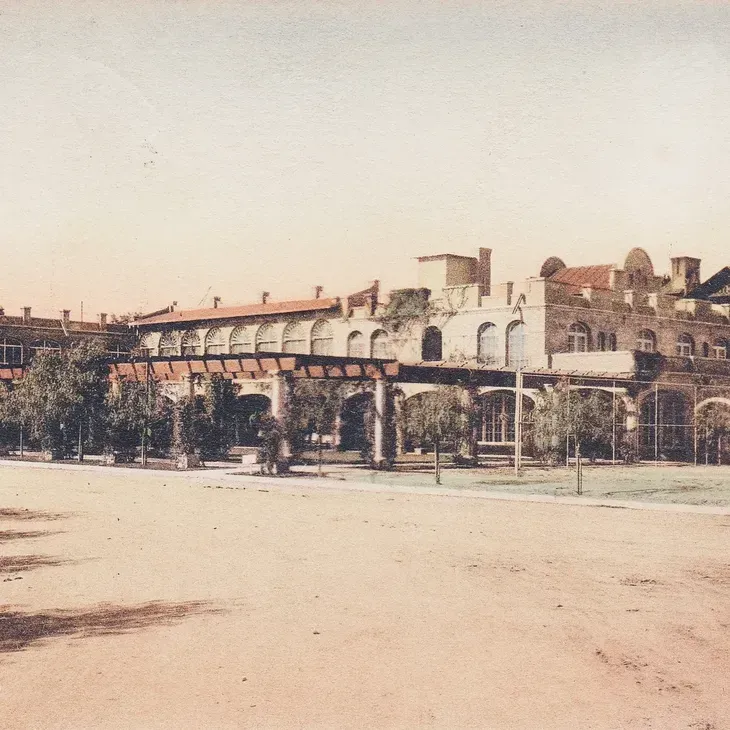 Old brick industrial building with arched windows and a covered walkway beside a sandy open lot