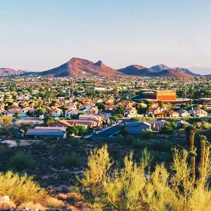 Sunlit desert cityscape with homes, a bright orange building, and red mountains in the distance