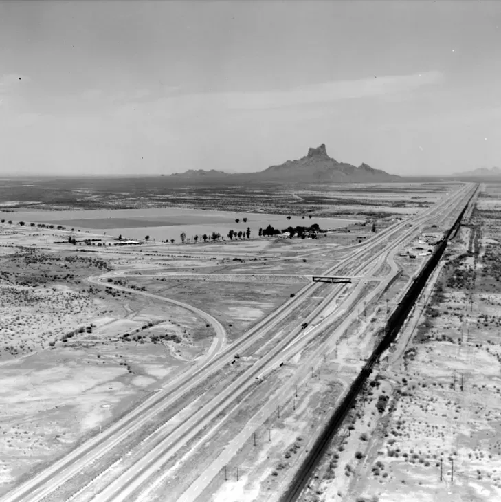 Railroad tracks cross a barren desert plain toward a distant butte under a cloudy sky