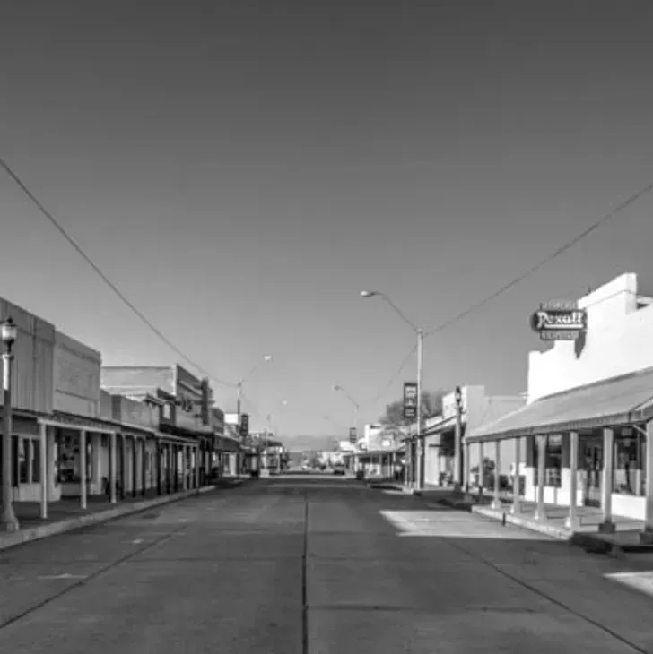 Empty small-town main street with storefronts on both sides in black and white.