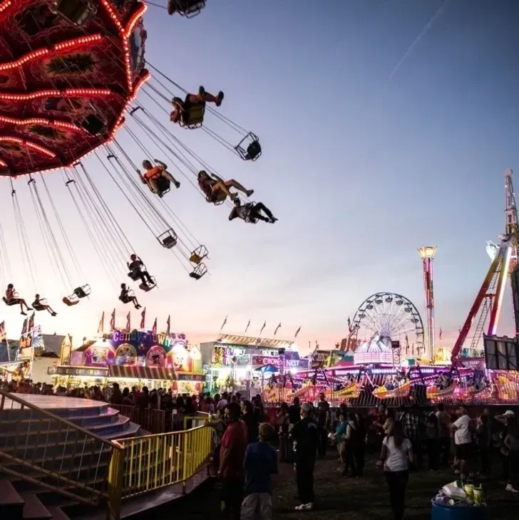 Evening carnival with a swinging ride, Ferris wheel, and a crowd under colorful lights