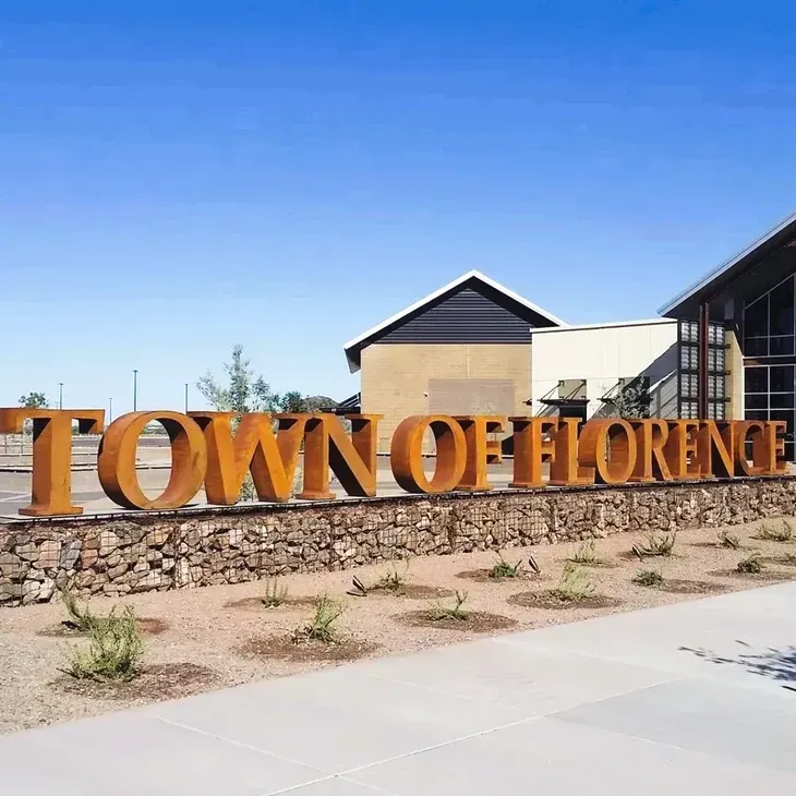 Town of Florence sign in large gold letters beside a stone wall under a clear blue sky