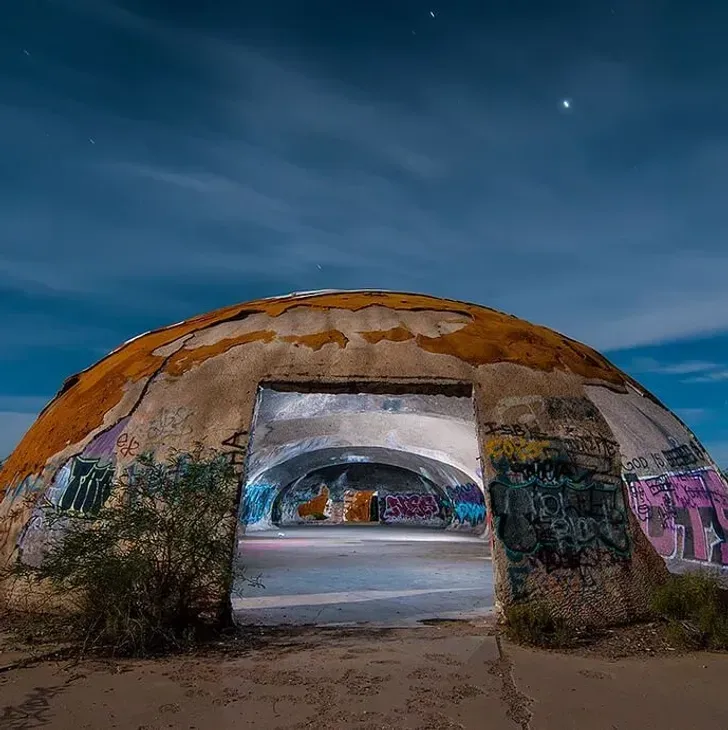Graffiti-covered concrete dome with a rectangular opening under a blue twilight sky