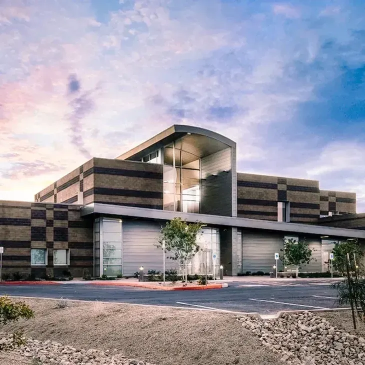 Modern office building exterior at dusk with glass entry and striped facade under a pastel sky