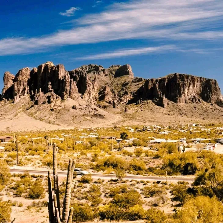 Desert landscape with rocky mountains, yellow scrub, and a blue sky with wispy clouds