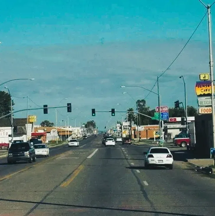 Busy urban street with cars at a traffic light under a clear blue sky.