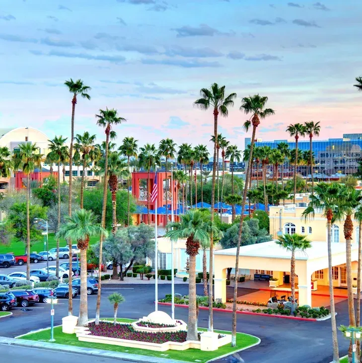 Palm-lined resort area with colorful buildings, parked cars, and a sunset sky.