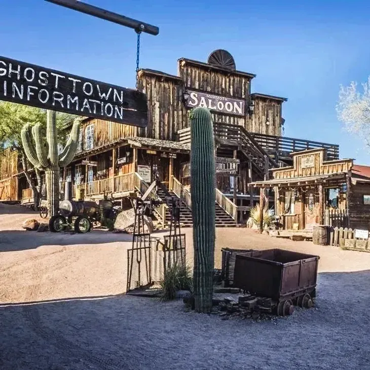 Ghost town saloon with weathered wooden buildings, cactus, and dusty desert street under a blue sky