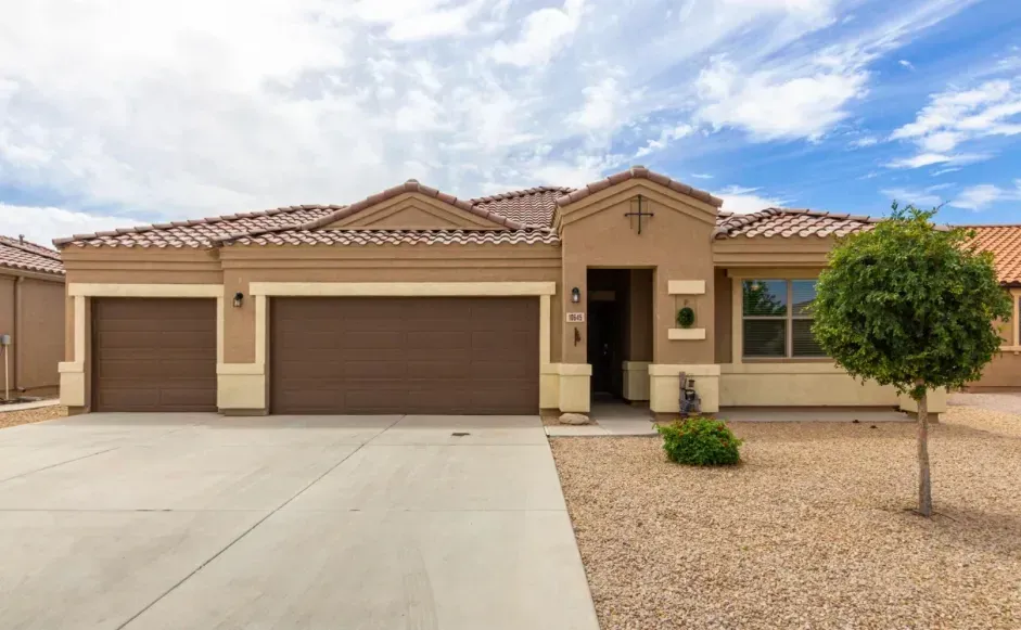 Single-story beige house with a three-car garage and desert landscaping under a blue sky