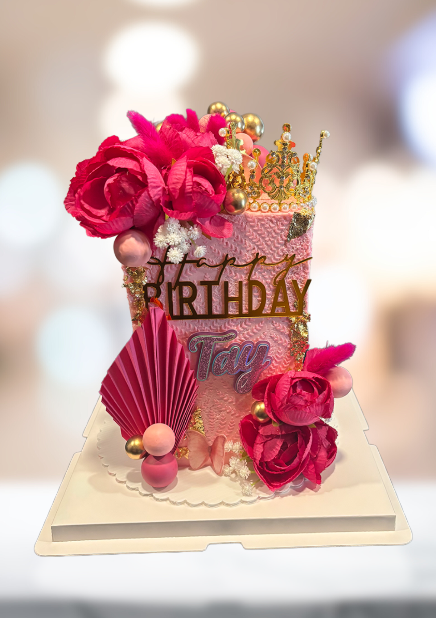 Pink and gold birthday cake topper with flowers, crown, and birthday message on a white base
