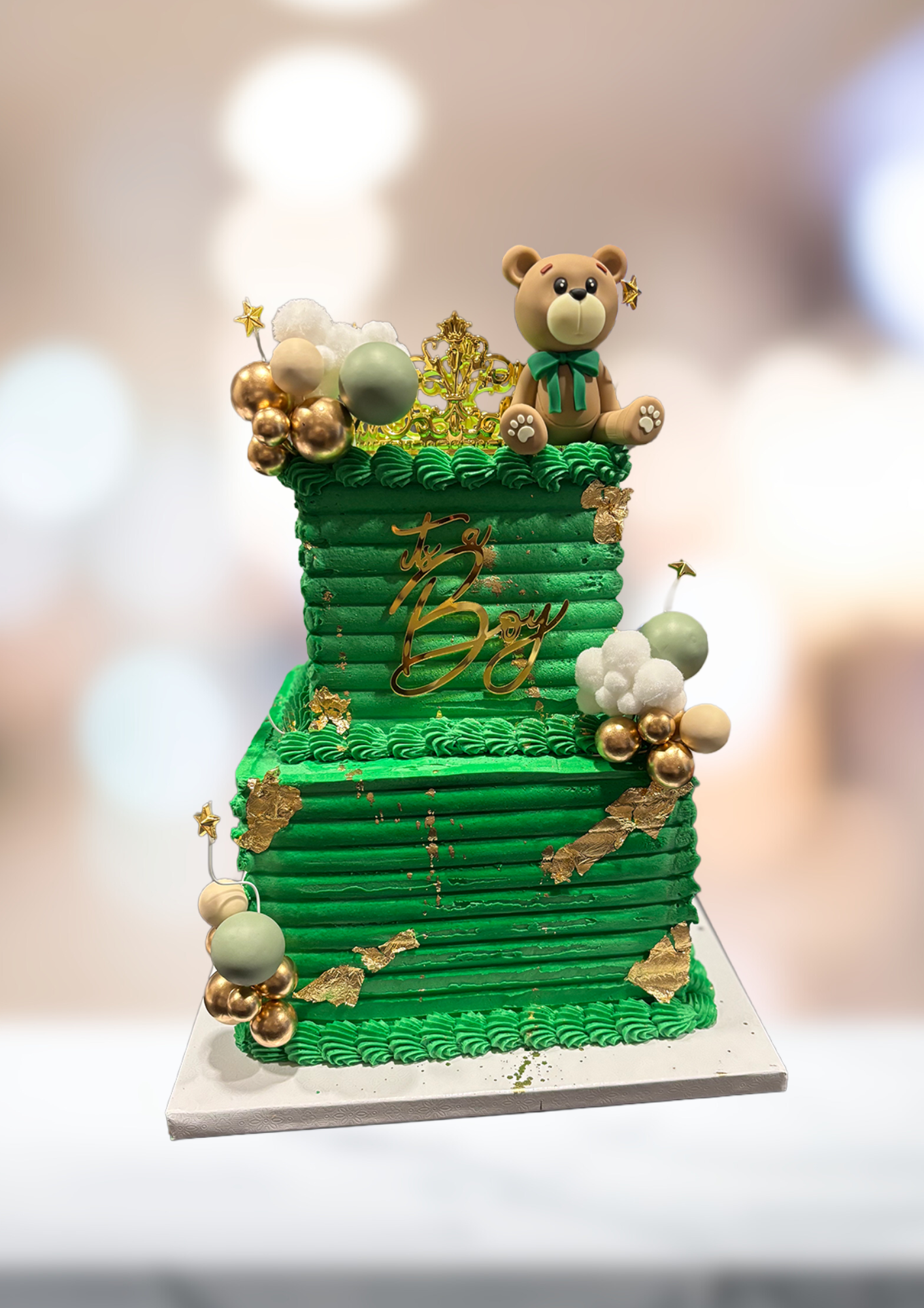 Green tiered cake with teddy bear topper and pearl-like decorations on a white stand