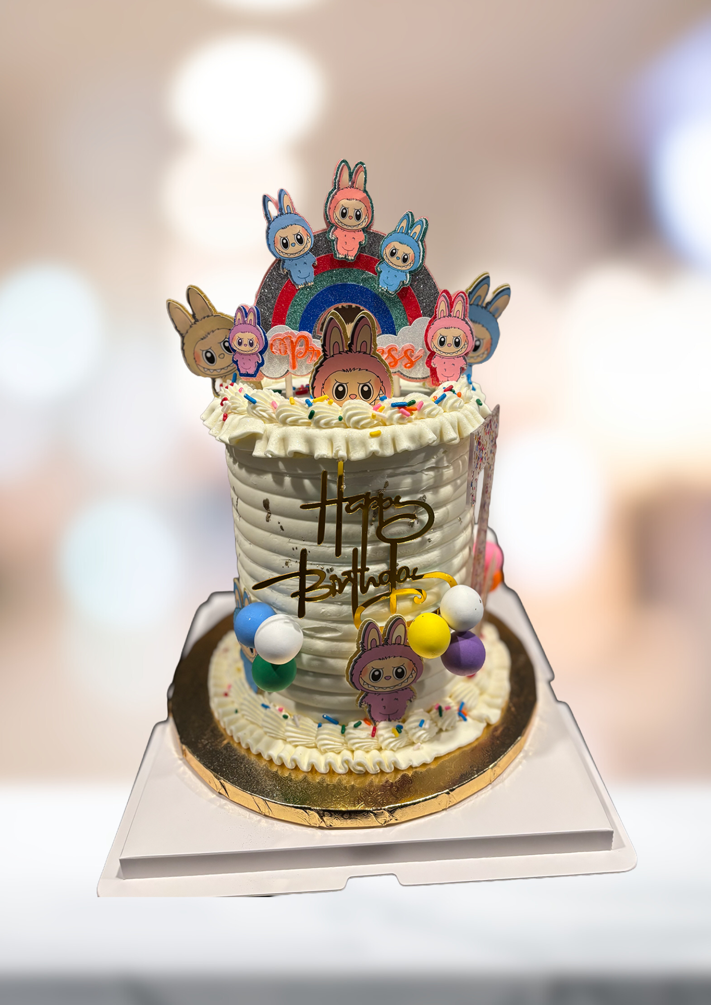 Decorated cake with colorful cartoon animal topper and gold accents on a clear stand